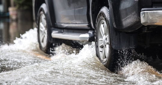Close up photo of a truck's tires driving on a flooded road.